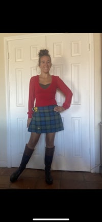a woman wearing a red sweater and a tartan skirt posing in front of a door