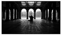 a black and white photo of a man sitting in an archway