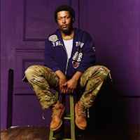 a man sitting on a stool in front of a purple wall
