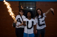 three young men posing in front of a brick wall with fire