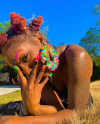a woman with colorful dreadlocks laying on the grass