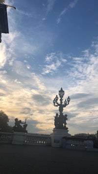 a statue in front of a building with clouds in the sky