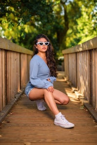 a woman crouching on a wooden bridge wearing sunglasses