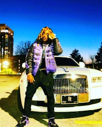 a man with dreadlocks standing next to a white car