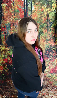 a girl in a black hoodie is posing in front of a forest