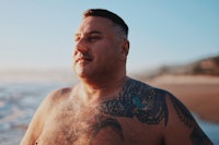 a man with tattoos standing on the beach