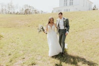 a bride and groom walking through a field in front of a white house