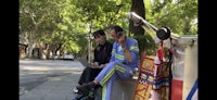 two men sitting on a bench talking on their cell phones