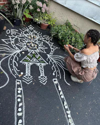 a woman drawing a rangoli on the ground