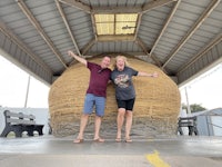 two people laying on top of a large hay bale
