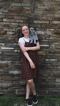a girl holding a stuffed animal in front of a brick wall