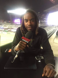 a man with dreadlocks sitting at a baseball stadium