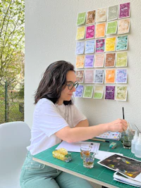 a woman sitting at a table with papers and paints