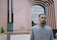 a man in a gray jacket standing in front of a building