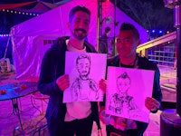 two men holding up their drawings at a festival