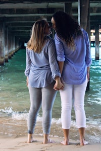 two women standing under a pier holding hands