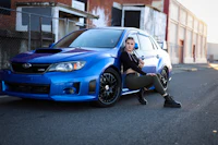 a woman posing next to a blue subaru wrx
