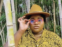 a woman wearing a hat and glasses in front of bamboo