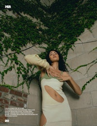 a woman in a white dress posing in front of an ivy covered wall