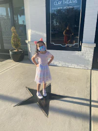 a little girl wearing a face mask standing in front of a star