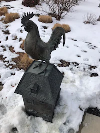 a rooster sits on top of a house in the snow