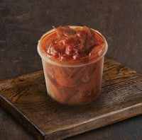 a plastic container with red sauce on top of a wooden board