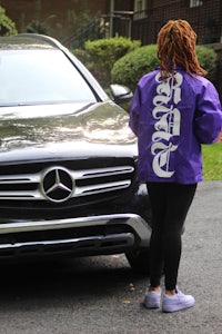 a woman wearing a purple jacket standing next to a mercedes benz