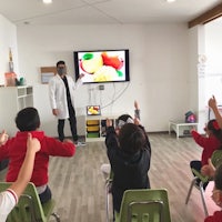 a group of children are sitting in front of a tv in a classroom