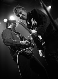 two men playing guitar on stage in black and white
