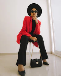 a woman in a red blazer and hat sitting on a chair