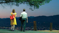 a man and woman standing on a hill overlooking a city