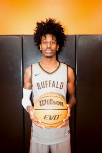 a young man holding a basketball in front of an orange wall