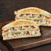 two grilled chicken sandwiches on a wooden cutting board