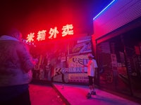 two people standing in front of a neon sign at night