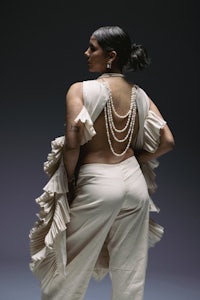 the back of a woman in a white jumpsuit with pearls
