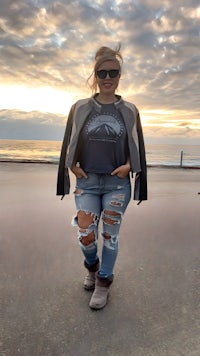 a woman in ripped jeans standing on the beach at sunset
