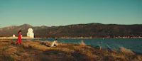 two people standing on a grassy area near a lake