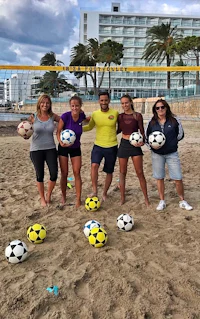 a group of people posing with soccer balls on the beach