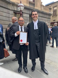 two men posing with a certificate in front of a building