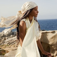 a woman in a white dress is standing on a rock next to the ocean