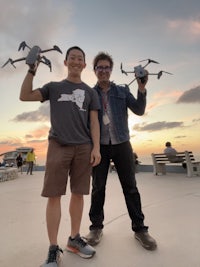 two men standing next to each other holding drones