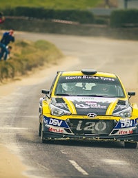 a yellow and black rally car driving down a dirt road