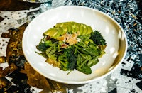 a bowl of greens and avocado on a silver tablecloth
