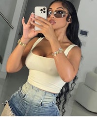 a woman taking a selfie in a white tank top and denim shorts