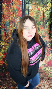 a woman in a black hoodie standing in front of a forest