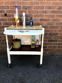a white bar cart with a bottle of liquor on it