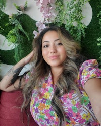 a woman sitting on a couch with a flower wall behind her