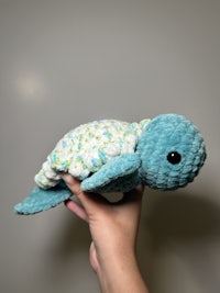 a person holding a blue crocheted stuffed animal