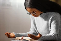 a young black woman is reading a book with a rosary in her hands