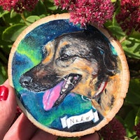 a person is holding a wood slice with a painting of a dog